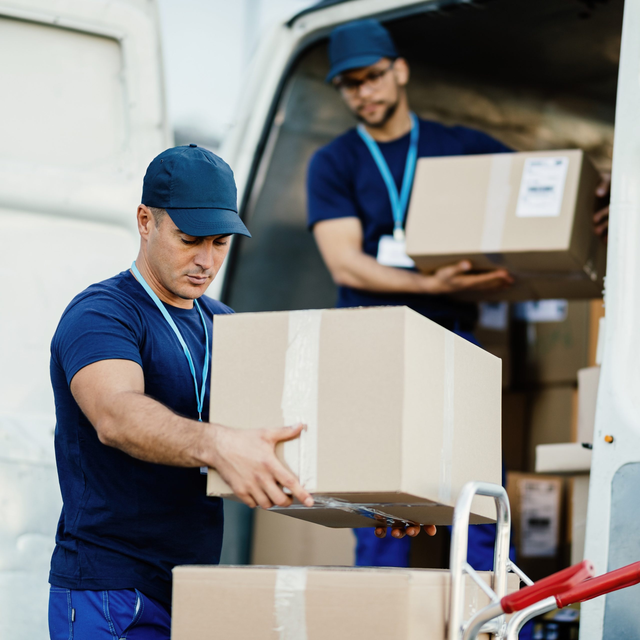 young courier his colleague unloading cardboard boxes from delivery van scaled